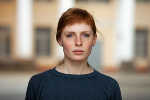 an image of a red haired woman in a blue shirt standing in front of a blurred out background